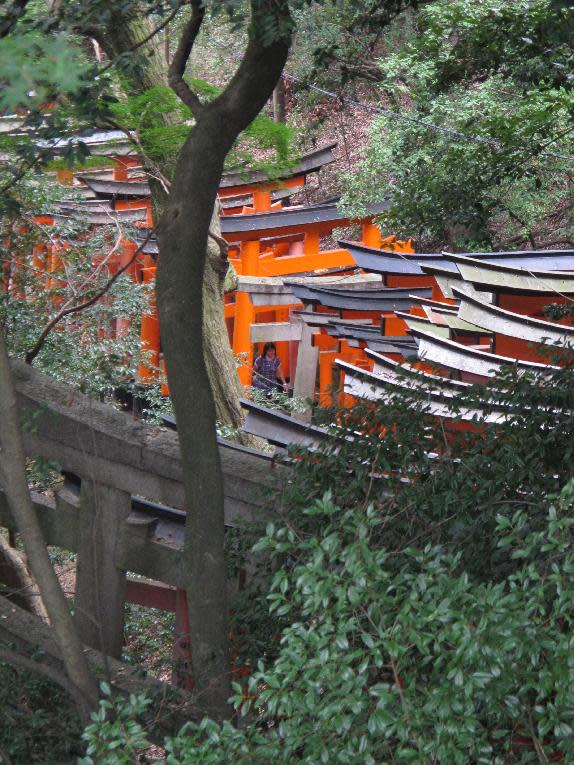 In this August 2012 photo, a visitor to the Fushimi Inari shrine in Kyoto, Japan, climbs steps through the shrine's gates. The shrine's main building sits within a minute of a train station, but a visitor could spend hours exploring the ancillary shrines situated along its pathways, with refreshment stops along the way. (AP Photo/Adam Geller)