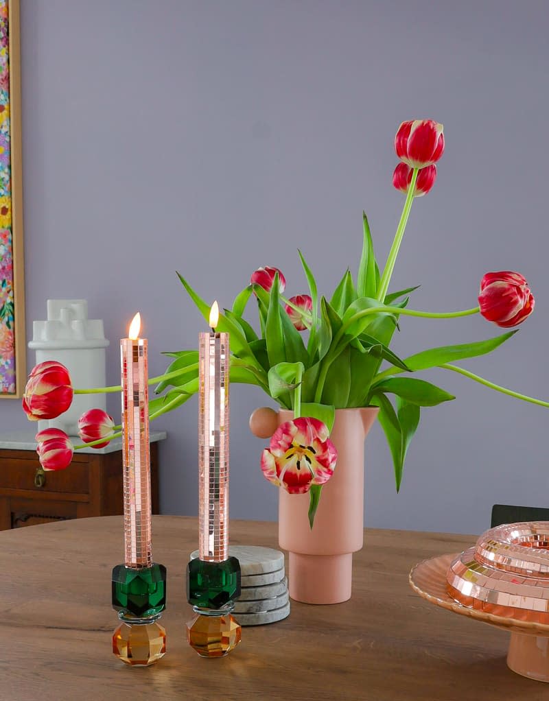 Pink candles and vase holding tulips sit on wood table.