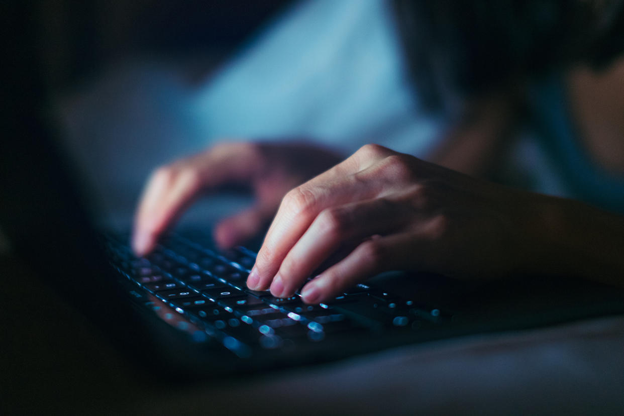 Close-up shot of female hands typing on computer keyboard, lying on bed, working late at home.