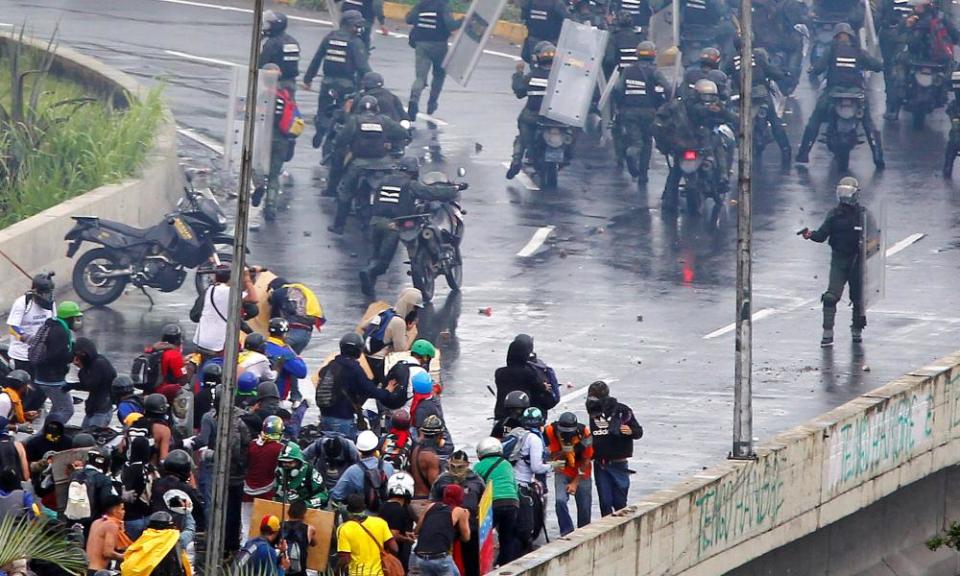 A member of the riot security forces points what appears to be a pistol towards a crowd of demonstrators during a rally.