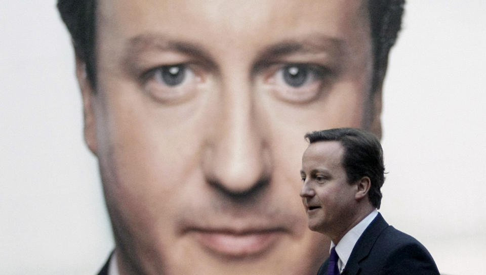 FILE - The leader of Britain's opposition Conservative party David Cameron walks past an image of himself after taking questions following a speech in London, Jan. 4, 2010. When Prime Minister Gordon Brown called the general election for May 2010, Labour, which had been in power for 13 years, its longest stretch in government, did better than expected and denied the Conservative Party, now led by the smooth David Cameron, a majority in the House of Commons. (AP Photo/Matt Dunham, File)