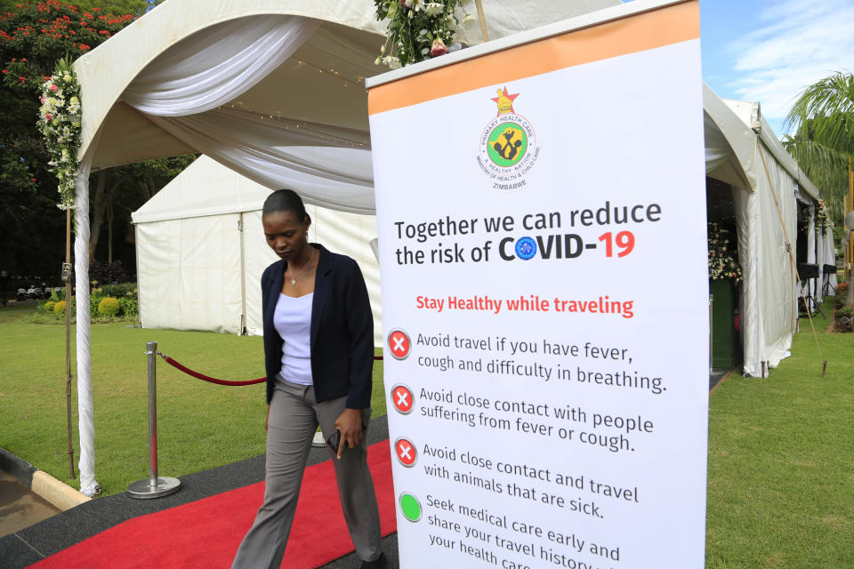 A woman walks past a coronavirus awareness campaign poster at State House in Harare, Thursday, March, 19, 2020. For most people, the new coronavirus causes only mild or moderate symptoms. For some it can cause more severe illness, especially in older adults and people with existing health problems. (AP Photo/Tsvangirayi Mukwazhi)