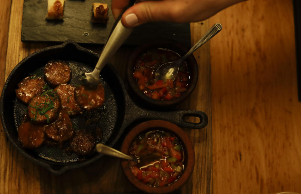 In this March 20, 2017 photo a tourist serves himself chorizo, the local sausage, at a dinner during an activity called "The Argentine Experience" in Buenos Aires, Argentina. Tourists participating in "The Argentine Experience" have the chance to learn about the local cuisine, wine and traditions during a dinner in Buenos Aires. (AP Photo/Natacha Pisarenko)