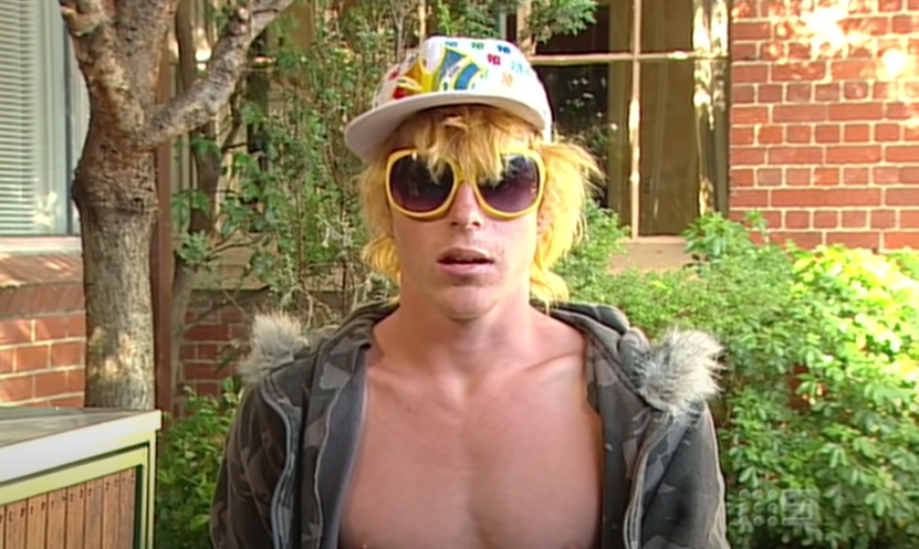 A bleach blond young guy in yellow sunglasses, colorful baseball cap, and wearing a hoodie with no shirt on