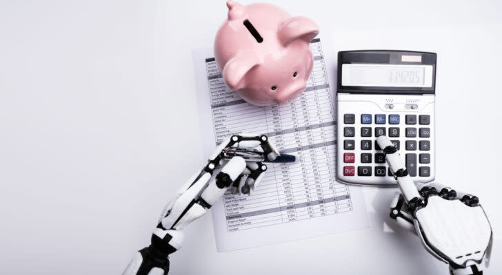 A concept image showing robotic hands with a calculator, financial form, and a pink piggy bank.