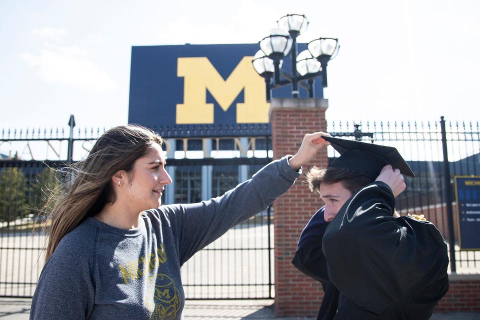 U-M senior Rita Sidhu helps adjust the cap for her friend Brian Galvin before they take graduation photos outside of the Michigan Stadium in Ann Arbor, Tuesday, March 17, 2020.