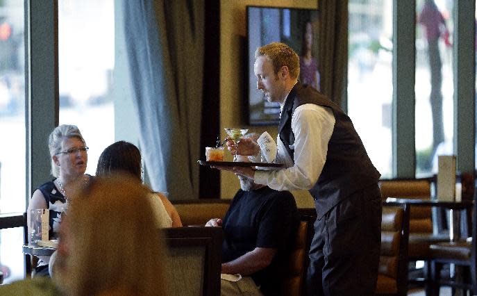 In this July 3, 2013, photo, a server brings drinks to guests in the newly-redesigned bar during "social hour" at a Sheraton hotel in Seattle. Long treated as dead spaces that hotel guests raced through on the way to the elevator, lobbies are being transformed into places to work, surf the Web or meet friends for a drink. (AP Photo/Elaine Thompson)