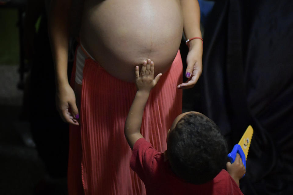 El sobrino de Ada Mendoza le toca el vientre de embarazada mientras está de pie en el departamento de sus padres donde vive con su pareja y siete familiares en el barrio Catia de Caracas, Venezuela, el jueves 27 de agosto de 2020. (AP Foto/Matias Delacroix)