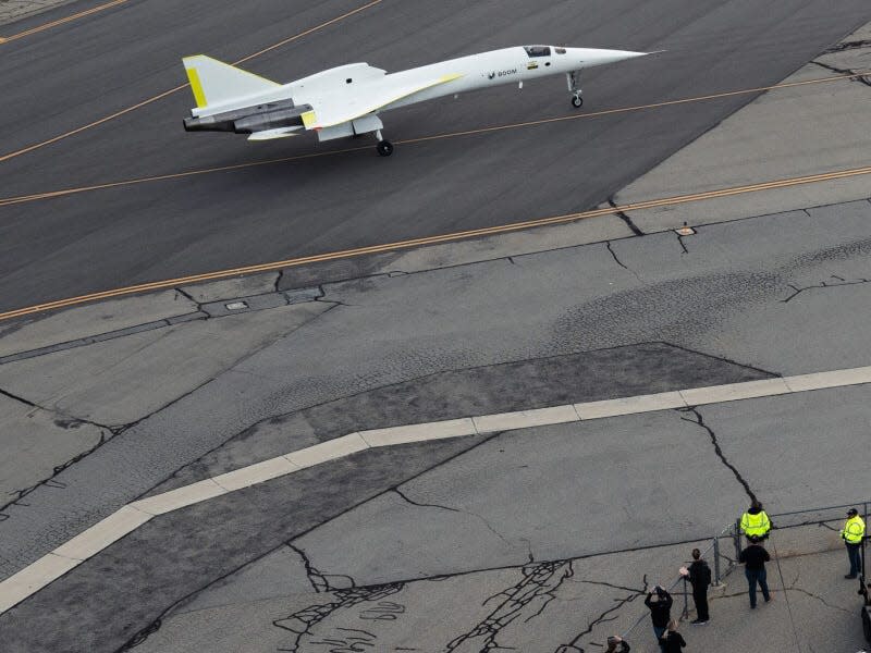 The XB-1 on the runway with people standing beside the gate taking photos.