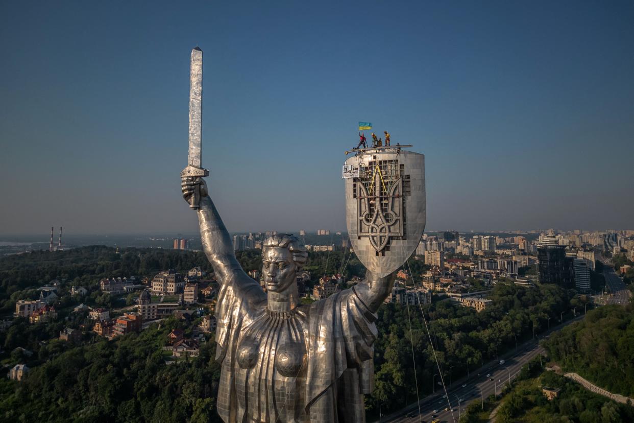 Steeplejacks wave the Ukrainian flag after finishing installing the coat of arms of Ukraine on the shield of the 62 metre Motherland Monument in Kyiv (AFP via Getty Images)