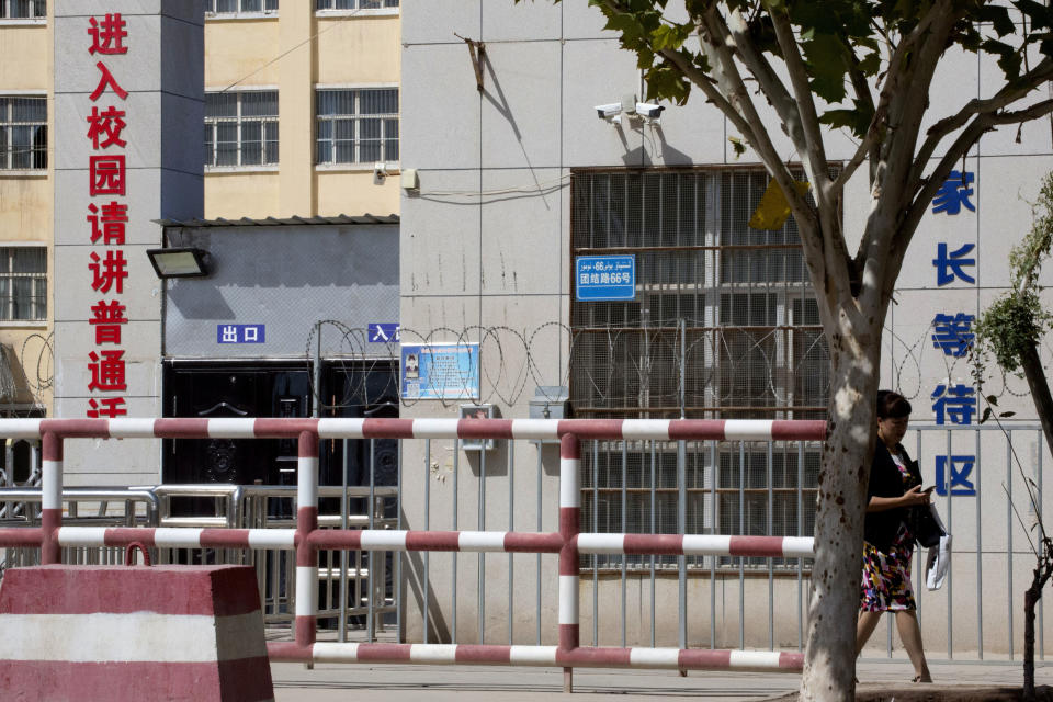 FILE - In this Aug. 31, 2018, file photo, a woman walks past the entrance to the No. 4 High School also known as the Peyzawat Bilingual High School with signs which read "Entering School Grounds, Please speak Mandarin," left, and "Parents Waiting Zone" in Peyzawat, western China's Xinjiang region. Australia and New Zealand on Tuesday, March 23, 2021 welcomed the United States, European Union, Canada and Britain taking joint action to impose sanctions on senior Chinese officials over human rights abuses in China’s far western Xinjiang region. (AP Photo/Ng Han Guan, File)