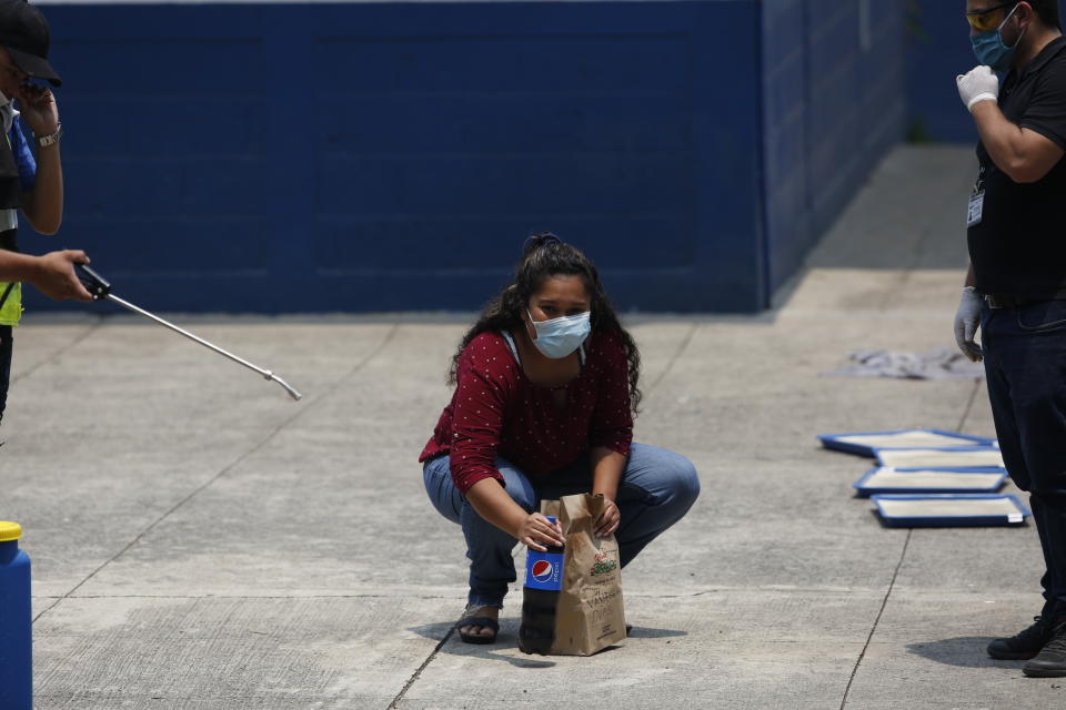 A deported woman looks at her family as she picks up the food they brought her, at the site where Guatemalans returned from the U.S. are being held in Guatemala City, Friday, April 17, 2020. The recently deported Guatemalans were placed in a athletic dorm facility to wait for the results of their tests for the new coronavirus. (AP Photo/Moises Castillo)
