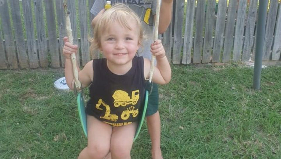 Blonde toddler sitting on swing smiling at the camera.