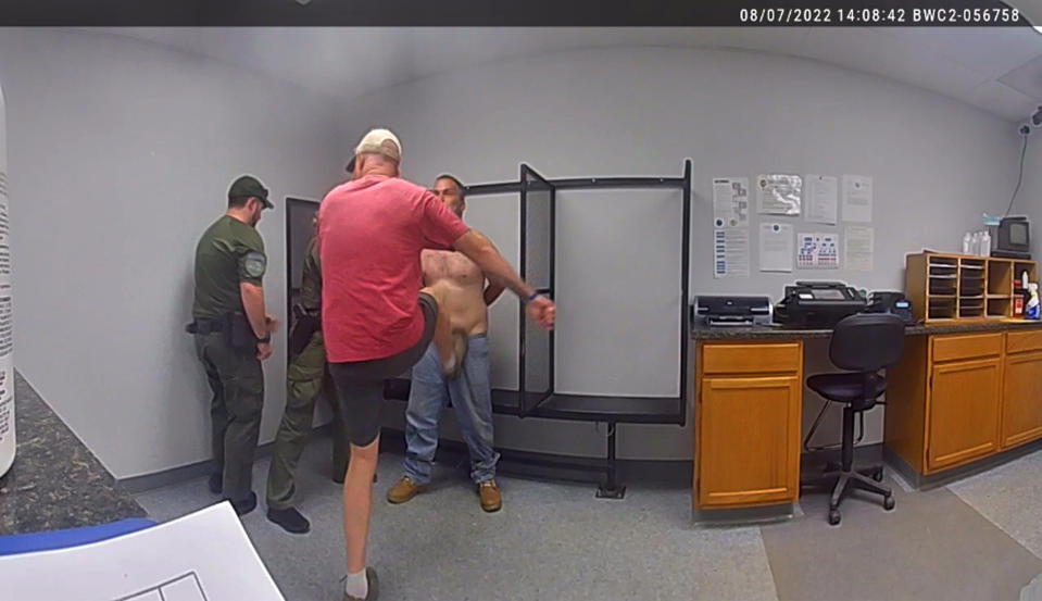 FILE - In this image taken from surveillance video provided by the Franklin County, Vt., sheriff's office, then-Sheriff Department Capt. John Grismore, at center wearing shorts, apparently kicks a handcuffed and shackled detainee in the groin on Aug. 7, 2022, in St. Albans, Vt. Grismore, a fired Vermont deputy sheriff who is the only candidate on the November ballot to become sheriff of the county where he served, was charged Friday, Oct. 21, 2022, with simple assault for kicking a shackled prisoner. (Franklin Co., Vt. Sheriff's Department via AP, File)