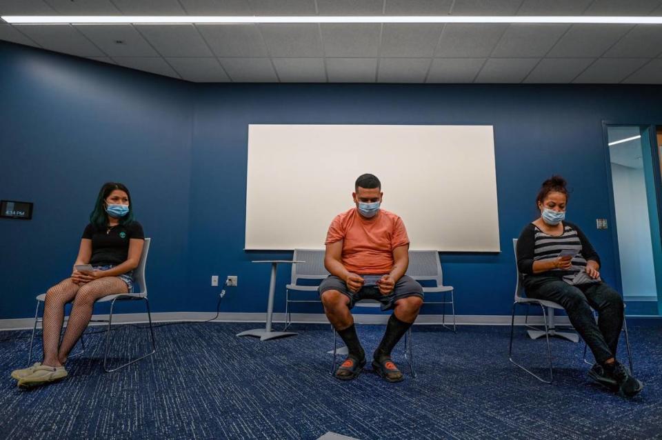 Holding their vaccination cards, Yency Fuentes Mejia, Kevin Perez Serrano and Ana Martinez, all of Kansas City, sat during a 15 minute waiting period after receiving a COVID-19 vaccination Thursday at a KC CARE Health Center clinic at the Northeast branch of the Kansas City Public Library.