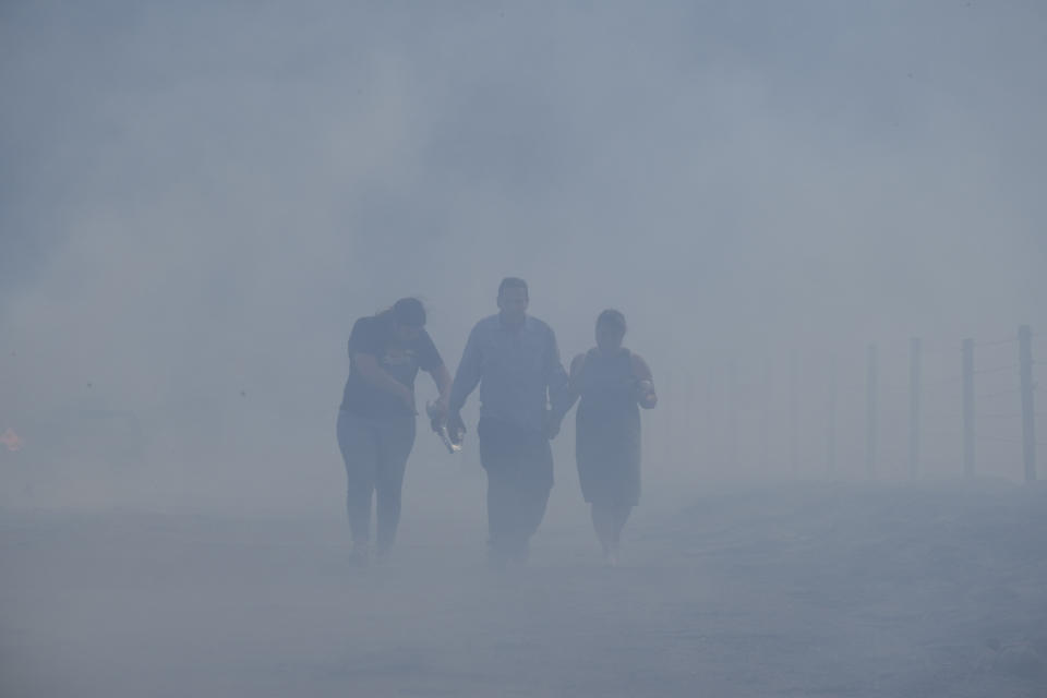 Homeowners Jose Lamas, center, his wife, Maria Covarrubias, right, and his daughter Astrid Covarrubias walk through the smoke after visiting their burned-out home from the South Fire in Lytle Creek, San Bernardino County, north of Rialto, Calif., Wednesday, Aug. 25, 2021. (AP Photo/Ringo H.W. Chiu)