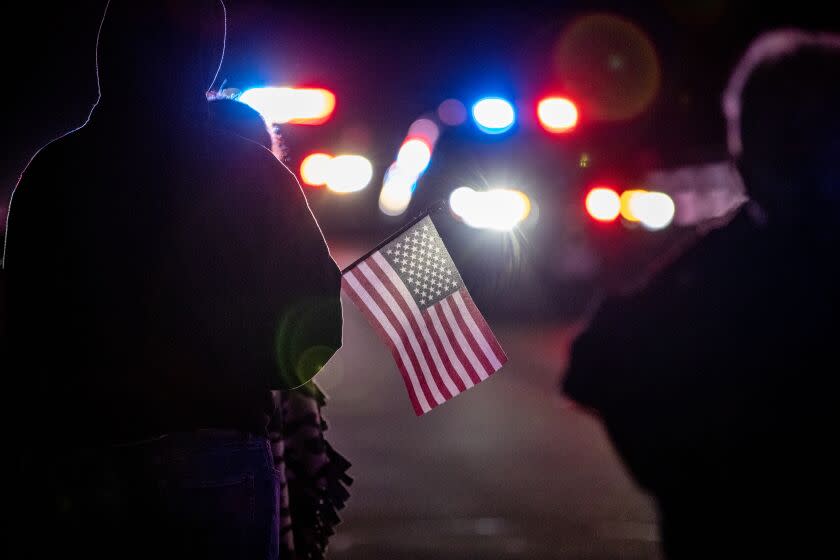 WILDOMAR, CA -JANUARY 13, 2023: A resident holds an American flag as a procession for fallen Riverside County Deputy Darnell Calhoun passes by from Inland Valley Medical Center on January 13, 2023 in Wildomar, California. Calhoun was killed in the line of duty responding to a domestic violence call in Lake Elsinore Friday afternoon(Gina Ferazzi / Los Angeles Times)