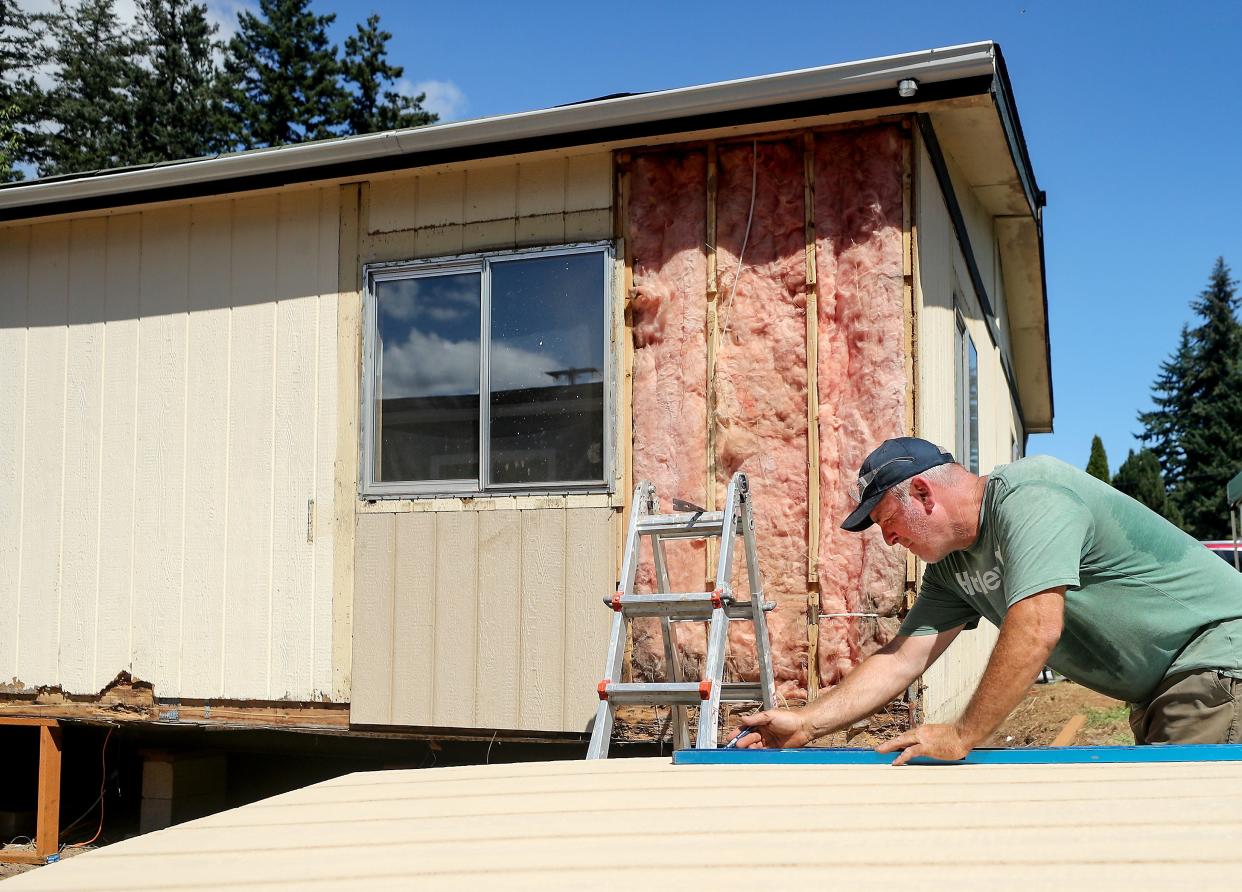 PSO Bluebills volunteer Jeff Young uses a straight edge as he prepares to cut a piece of new exterior siding to fit into place on the home behind him at the Poulsbo Mobile Home Park on Thursday, July 27, 2023.