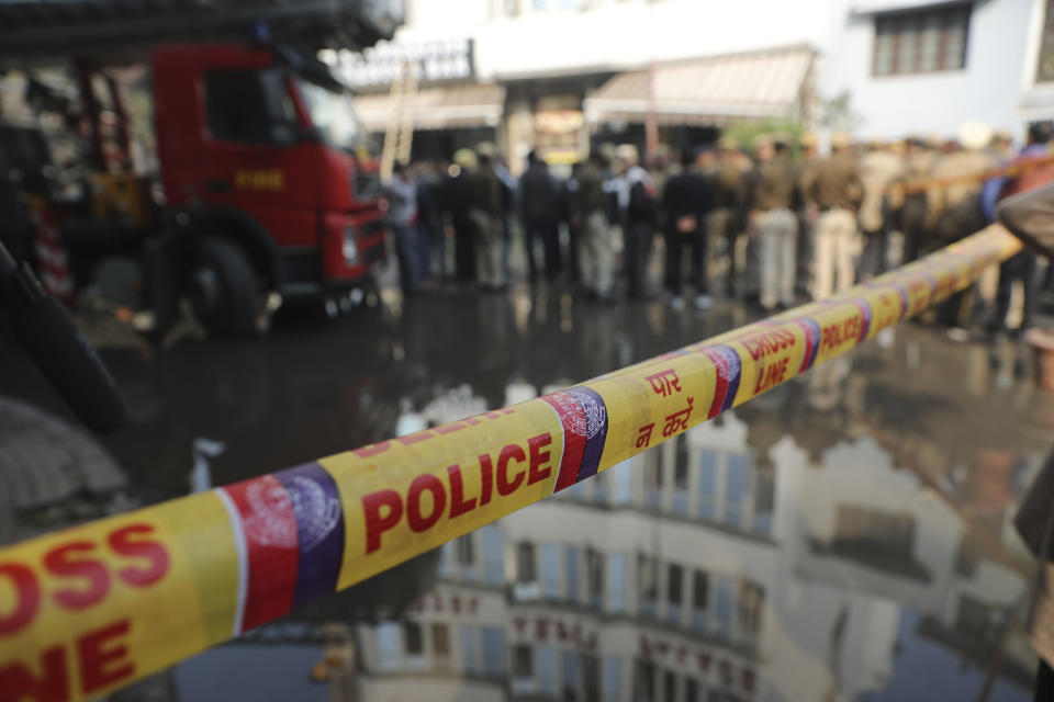 Policemen and others stand at the spot after an early morning fire at the Arpit Palace Hotel killed more than a dozen people in the Karol Bagh neighborhood of New Delhi, India, Tuesday, Feb.12, 2019. (AP Photo/Manish Swarup)