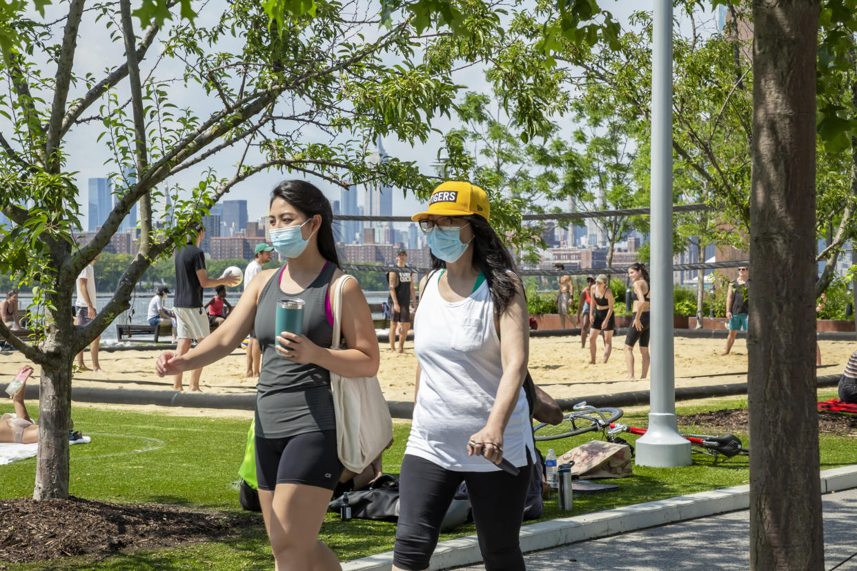 Two young women wear protective face masks to stop the spread of COVID-19 as they walk past the volley ball court at Domino Park in North Williamsburgh, Brooklyn, New York.