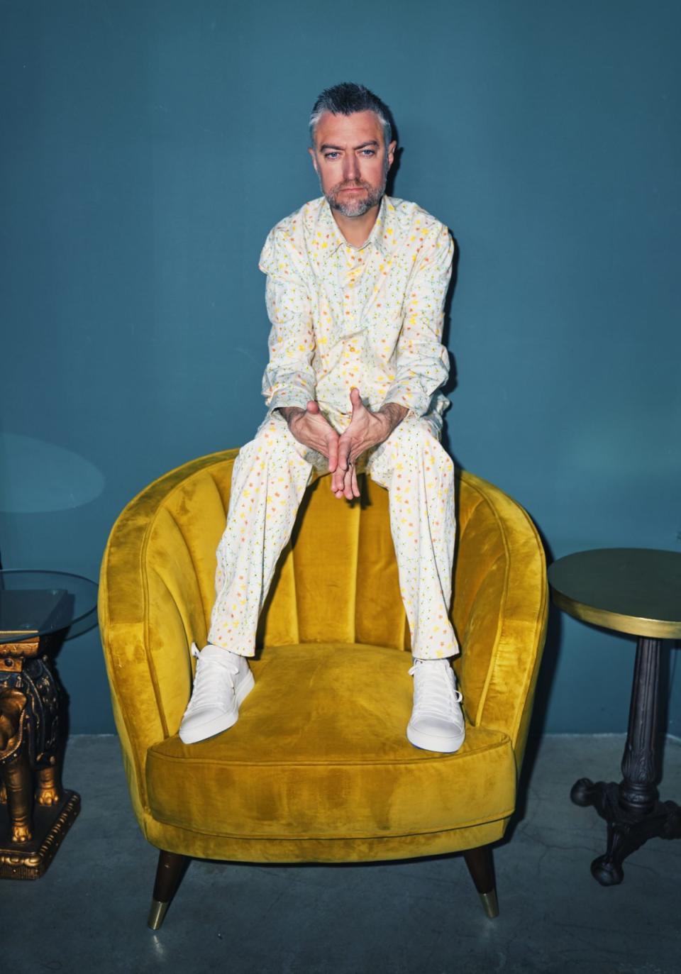 Portrait of Sean Gunn in a white suit on a yellow chair against a blue wall