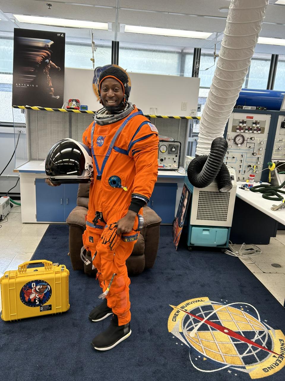 an astronaut standing up in a spacesuit and smiling, inside an office