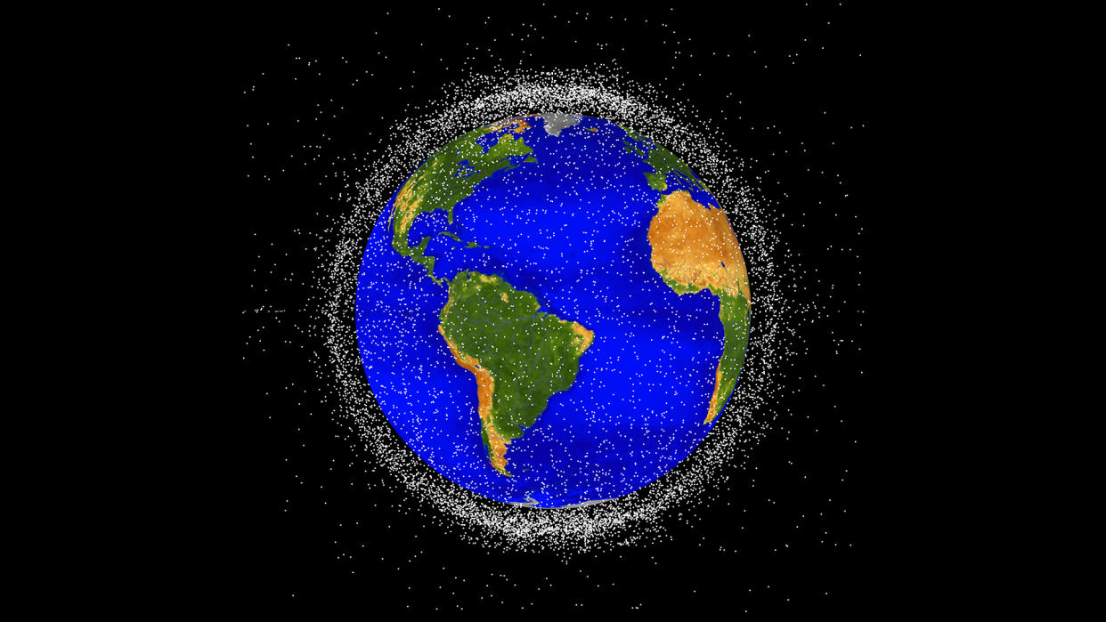  The space junk appears as many small white points surrounding Earth, which has bright blue oceans and green and brown continents.  The space junk is thick enough to form a cloud that obscures most of the black background when viewed from the edges around Earth. 