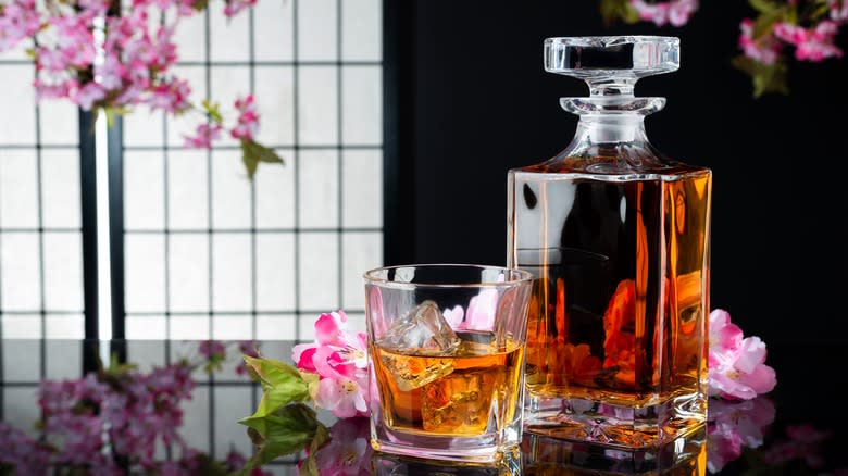 A bottle and glass of Japanese whisky next to pink flowers