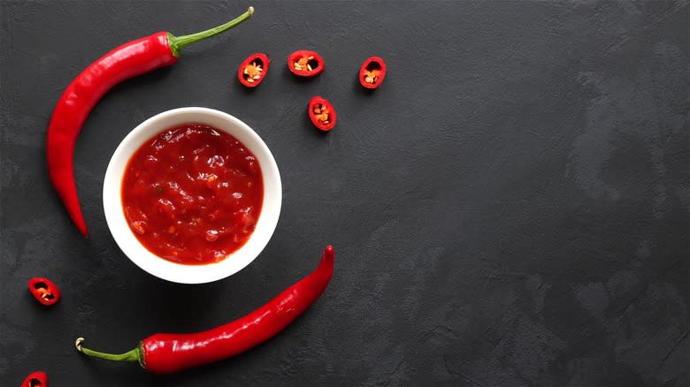 Whole and chopped red chili peppers on counter with dish of jelly