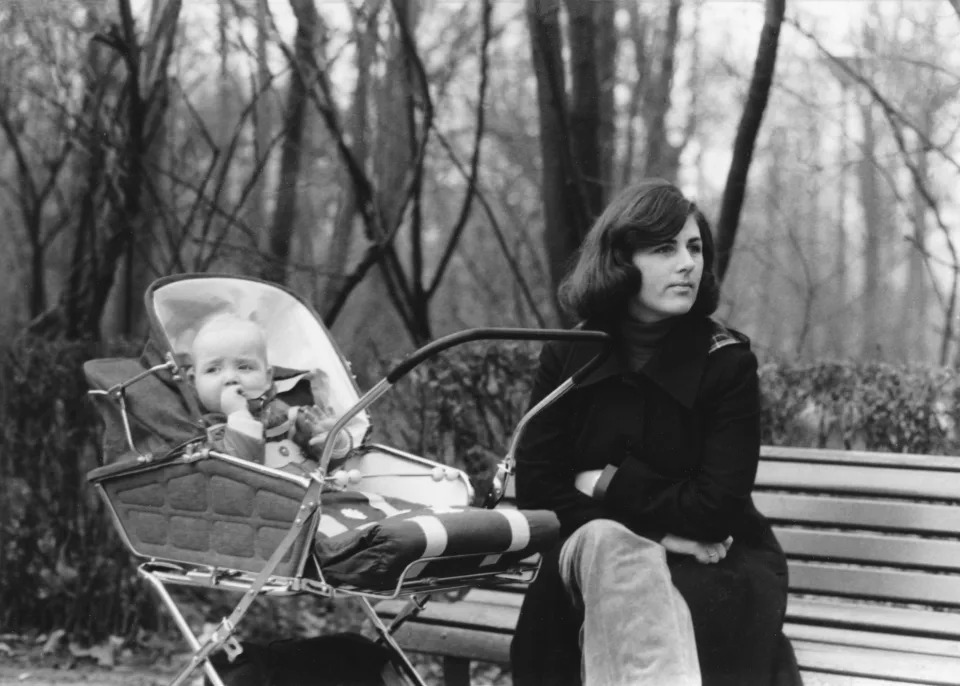 pensive woman in a park looking away from her baby in a stroller