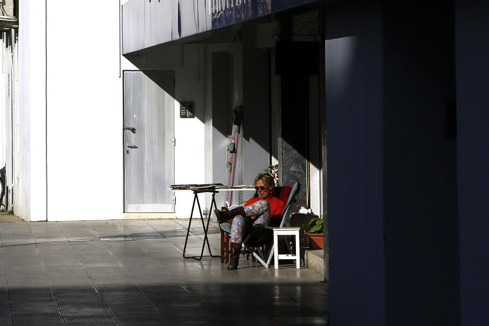 A woman sits in the sun and reads a book outside a shop in central capital Nicosia, Cyprus, Friday, March 12, 2021. Cyprus put the breaks on a wider loosening of COVID-19 restrictions by keeping middle school students at home for two more weeks as the infection rate remains high partly because of how widespread the U.K. variant has become. (AP Photo/Petros Karadjias)