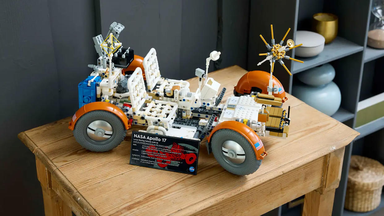  A white and orange four-wheeled lego rover sits on a small wooden table. 