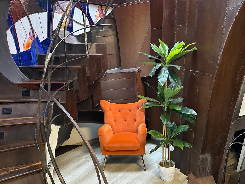 Spiral staircase with an orange chair and a plant in nook and stained-glass windows next to stairs