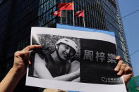 A protester holds a photo of Chow Tsz-Lok during a memorial flash mob to remember him near Chinese and Hong Kong flags in Hong Kong on Friday, Nov. 8, 2019. Chow, a Hong Kong university student who fell off a parking garage after police fired tear gas during clashes with anti-government protesters died Friday, in a rare fatality after five months of unrest that intensified anger in the semi-autonomous Chinese territory. (AP Photo/Vincent Yu)