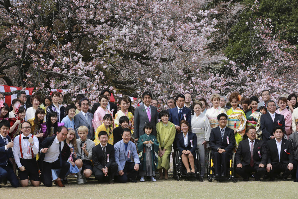 FILE - In this April 15, 2017, file photo, then Japanese Prime Minister Shinzo Abe, center with a pink tie, pose with Japanese artists, entertainers, athletes and other guests during a cherry blossom viewing party hosted by Abe at Shinjuku Gyoen National Garden in Tokyo. On Friday, Sept. 18, 2020, Japanese police arrested a man, who was invited to one of annual cherry blossom viewing parties hosted by the former Prime Minister Abe, in a massive fraud involving thousands of elderly customers(AP Photo/Eugene Hoshiko, File)