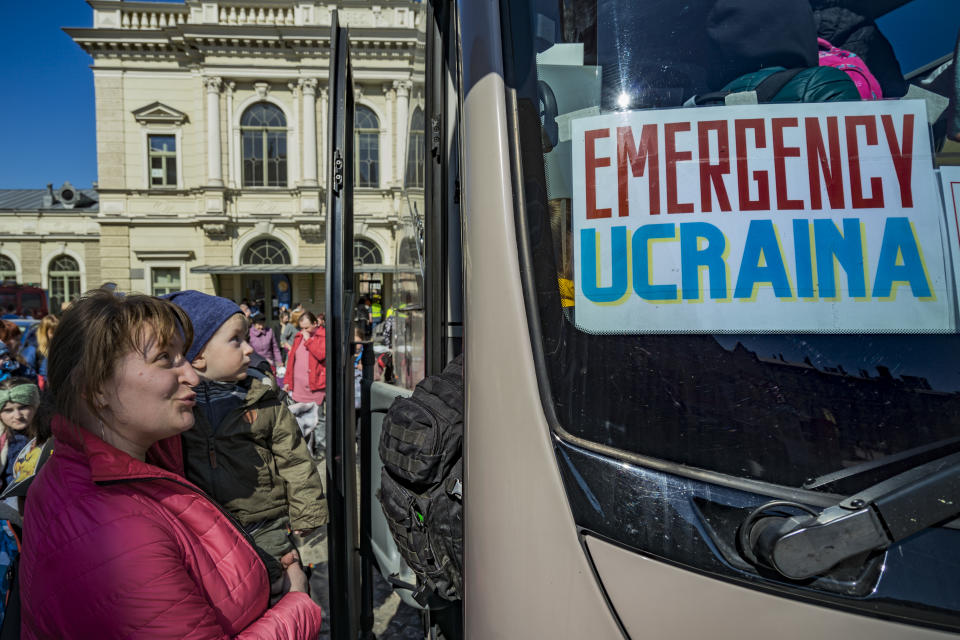 A woman holding a young child board a bus with a sign reading: Emergency Ucraina.