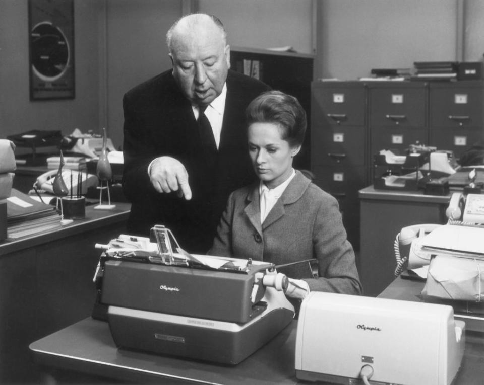 he stands behind her as she sits at a typewriter