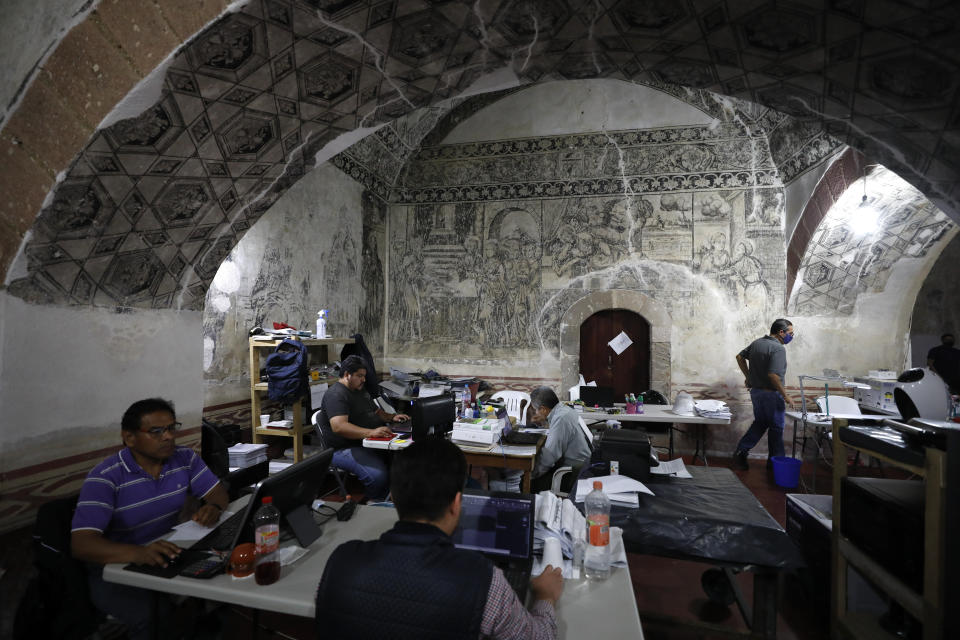 Employees of the construction company entrusted with the restoration of the former San Juan Bautista Convent work at desks set up beneath painted vaults in a building adjacent to the church that was damaged in a 2017 earthquake, in Tlayacapan, Morelos state, Mexico, Tuesday, Oct. 13, 2020. The convent was started in 1554, soon after the conquest. (AP Photo/Rebecca Blackwell)
