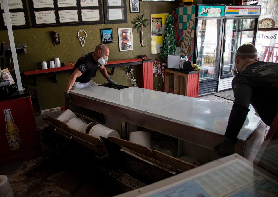 Jeff Weigel and his son Noah lift their ice cream cooler that was overturned in the storm surge from Hurricane Ian at their restaurant, The Sanibel Deli & Coffee Factory on Thursday, Oct. 20, 2022. The two spent the day cleaning up and plan to return daily to get the restaurant back up and running as soon as possible.