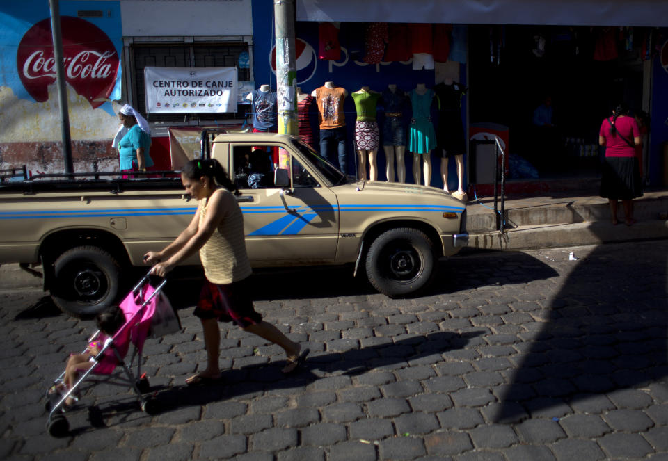 In this Aug. 18, 2018 photo, people walk past a general store in Intipuca, El Salvador. In Intipuca, immigrating to the U.S., particularly Washington D.C., has been a way of life for 50 years, leaving many of its homes empty due to half the town's population living in Washington D.C. (AP Photo/Rebecca Blackwell)