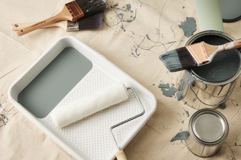 paint scattered on a canvas with paint can, paint roller and tray, and brushes around