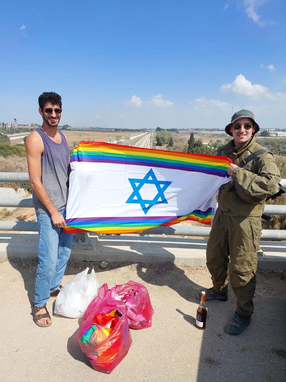 Nadav Yitzhaki and Yoav Atzmoni  holding an Israeli flag with LGBTQ+ colors
