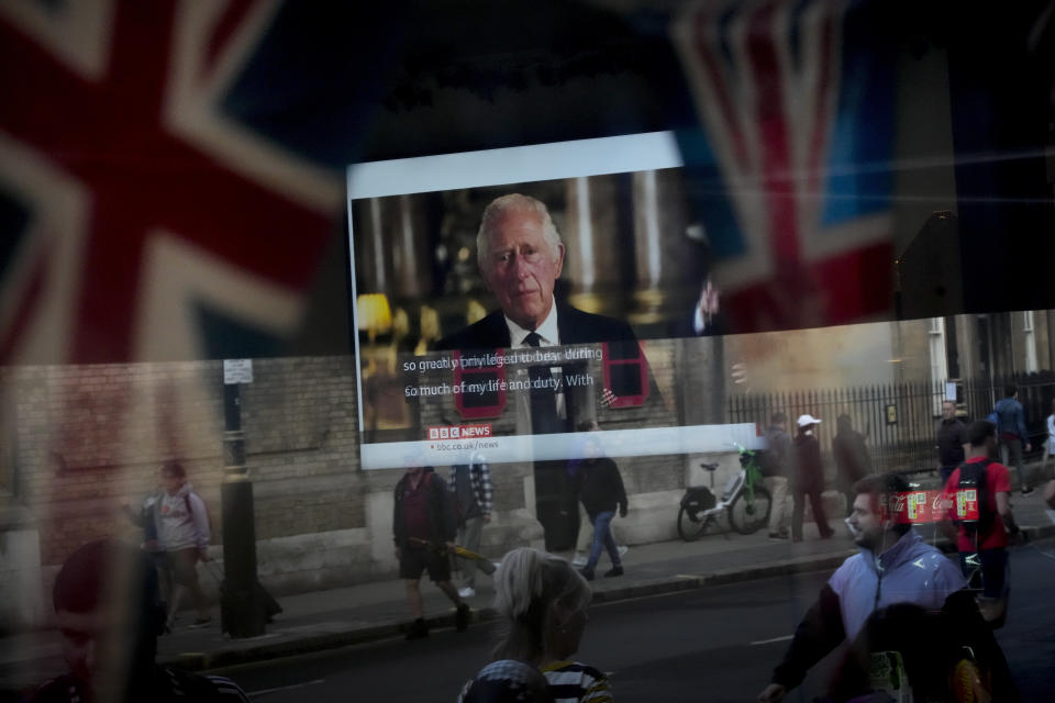 FILE - The televised speech of the new King Charles III is seen through the window of a pub as passer-bys are reflected in London, Friday, Sept. 9, 2022. (AP Photo/Christophe Ena, File)