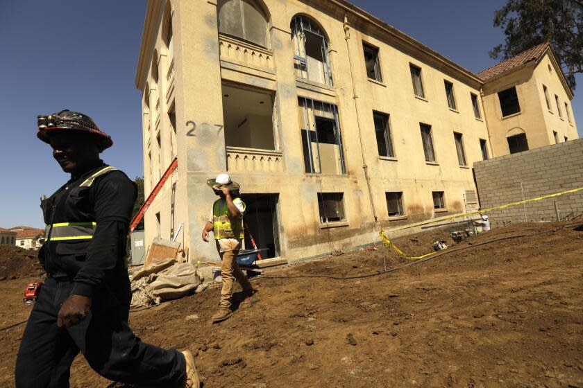 LOS ANGELES, CA - JUNE 23, 2022 - - Construction workers walk past Building 207 that is being refurbished as housing for veterans on the Veteran Affairs West LA campus in Los Angeles on June 23, 2022. This is the Collective's first project, a 60-unit building for senior veterans and their families and is scheduled to open this fall. Along with U.S. VETS, the Collective is made up of Century Housing, a nonprofit that builds and finances affordable housing, and Thomas Saffran and Associates, a Brentwood-based for-profit affordable housing developer. The master plan calls for 14 buildings to be brought up to current standards but preserved in their original form with another 14 built from the ground up. (Genaro Molina / Los Angeles Times)