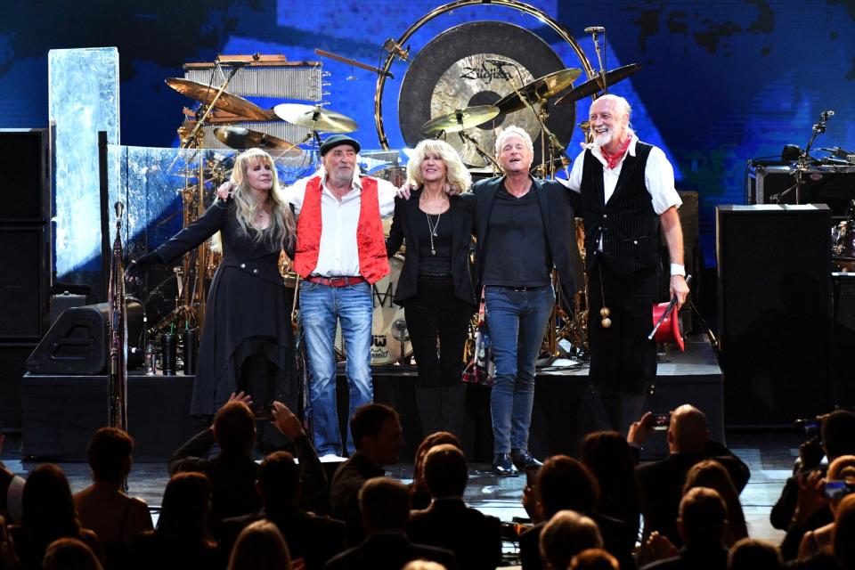 Two women and three men stand and smile with their arms around each other on a stage