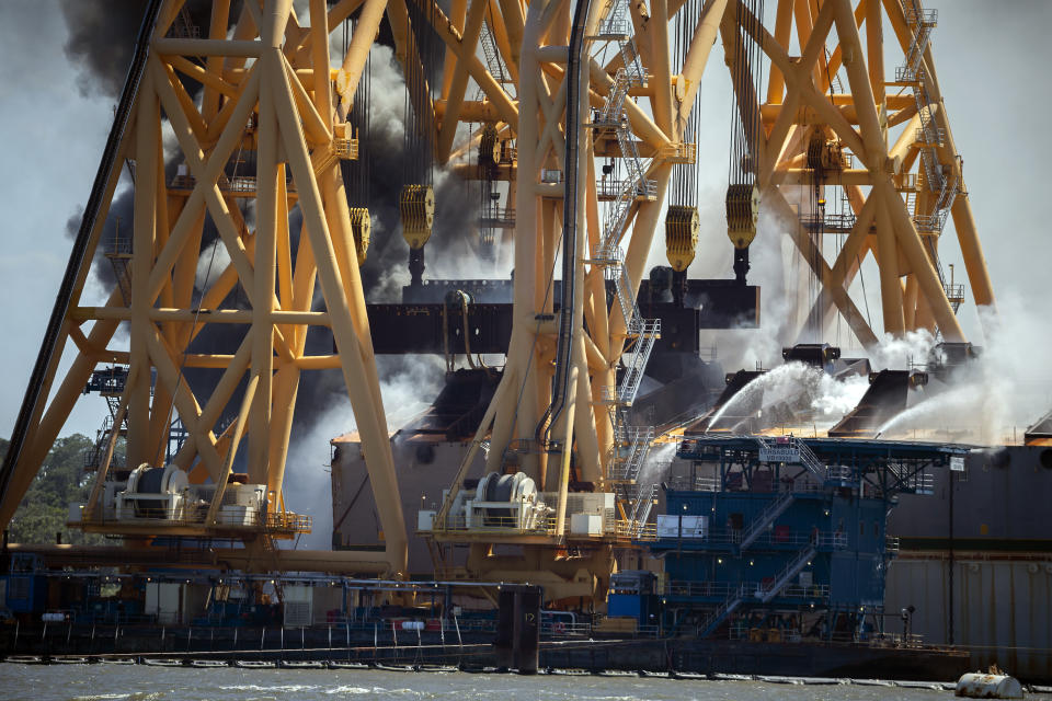 Firefighters working from the towering crane being used to dismantle the ship, hose down a fire in the overturned cargo ship Golden Ray, Friday, May 14, 2021, Brunswick, Ga. The Golden Ray had roughly 4,200 vehicles in its cargo decks when it capsized off St. Simons Island on Sept. 8, 2019. (AP Photo/Stephen B. Morton)