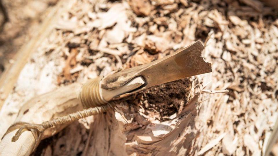 A Bronze Age replica tool with a wooden handle resting on the log