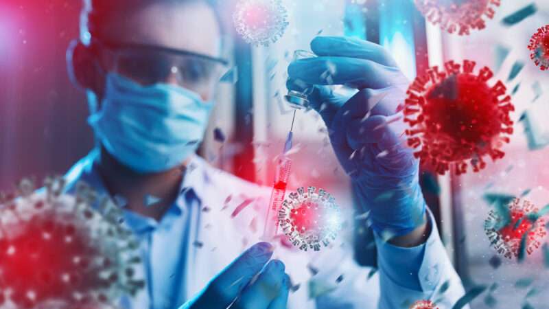 A scientist in a mask holds a test tube with enlarged depictions of COVID-19 across the image