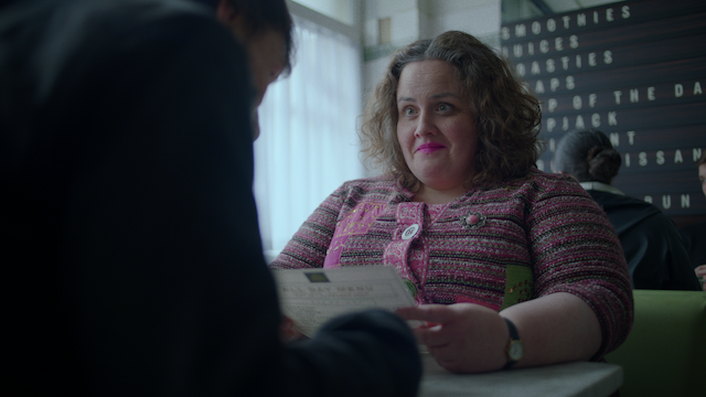 Jessica Gunning, sitting and holding a menu, like Martha in 