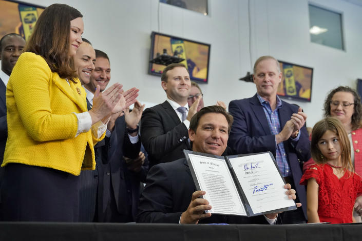 DeSantis, seated in front of a dozen supporters, holds up a signed bill.